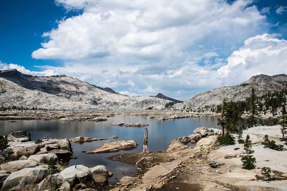 Blue lake strewn with rocks in the Sierras with partly cloudy sky