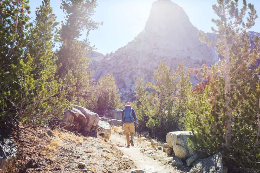 man walking on trail in high sierra with large granite cliff faces around him