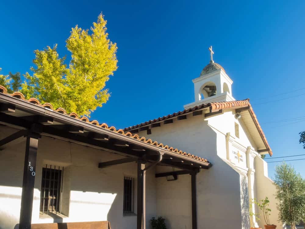 white church building with bell tower and cross and adobe roof in santa cruz