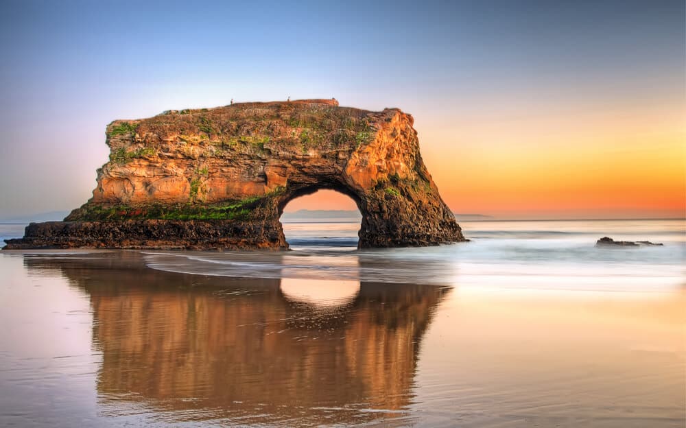 Natural Bridges State Beach - a rock arch as the tide goes out in santa cruz at sunset with briliant orange and blue sky