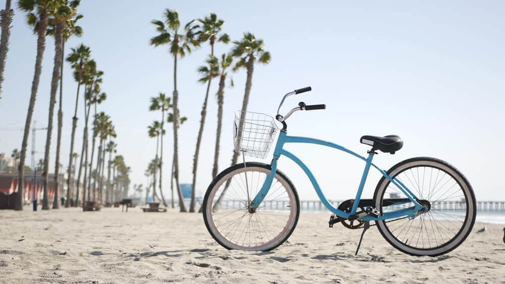 Blue bicycle, cruiser bike by sandy ocean beach, pacific coast near Oceanside pier. Vintage cycle, tropical palm trees, lifeguard tower watchtower hut