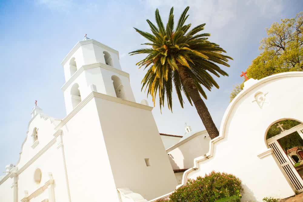 View of Historic San Luis Rey Mission in Oceanside California. White Spanish Colonial style church and palm tree.
