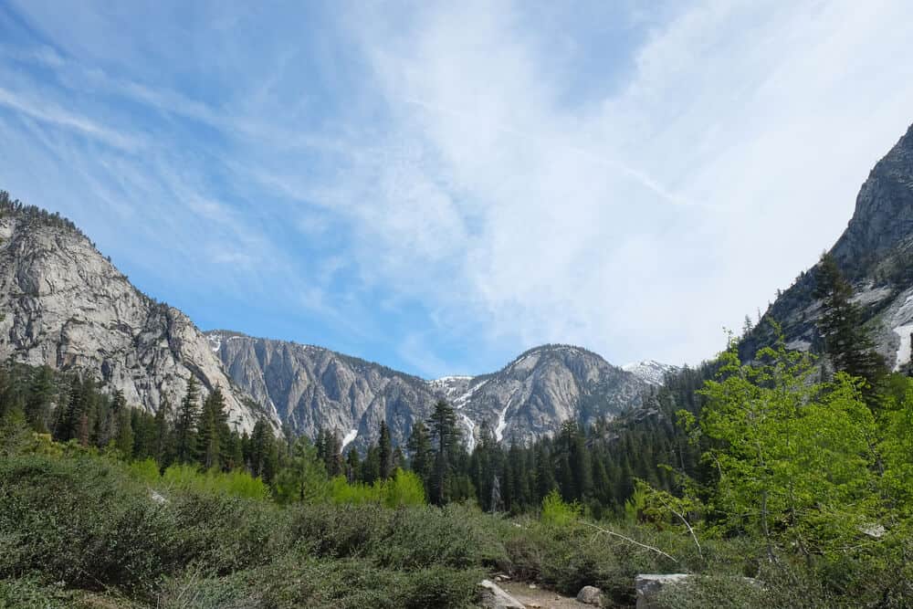 Granite mountains towering above the valley of Paradise Valley along the Rae Lakes Loop with a partly cloudy sky above.