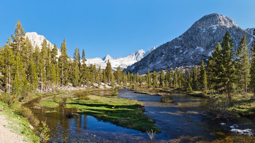 Bubbs Creek in Kings Canyon National Park and Forester Pass in the Distance. Creek surrounded by mountains marked wth small pockets of snow and pine trees.