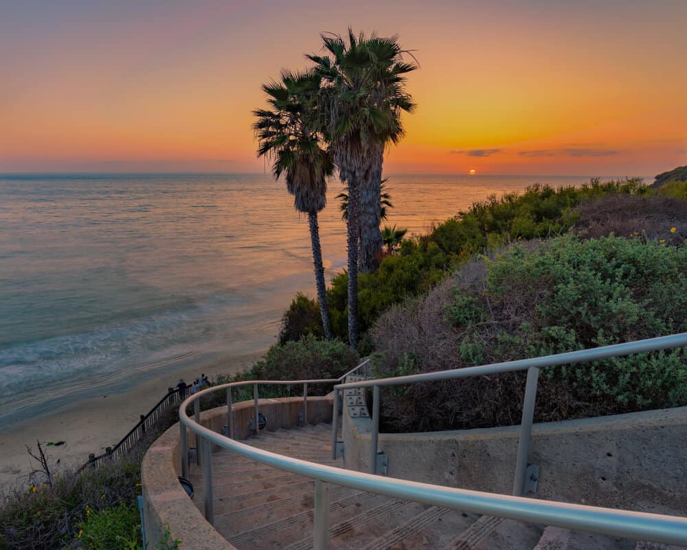 sunset views over the pacific ocean with a cluster of palm trees, a winding staircase, and a beach at swamis in encinitas.