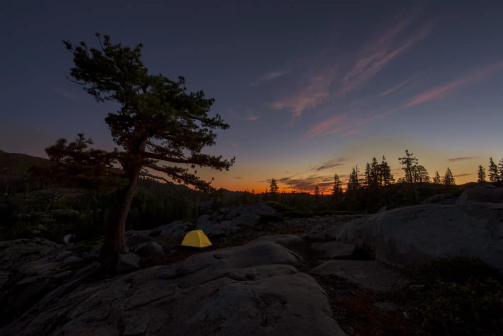 A yellow tent against dark landscape with a set sun and the last remnants of sunset light.