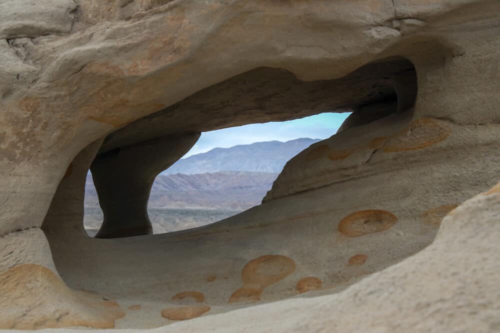 Water and Wind Carved Caves in the Corrizo Badlands Wind Caves, showing a gap in the rock from which you can see mountains in the distance.