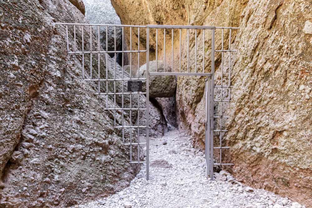 An open gate leading to Balconies Cave, with a rock balanced between other larger rocks