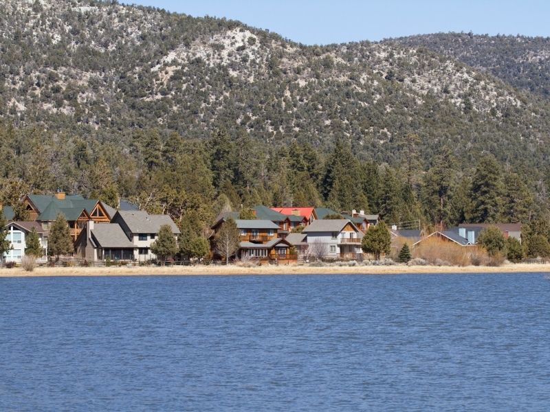 lake shore with houses on the edge of the lake with large mountains behind the houses.