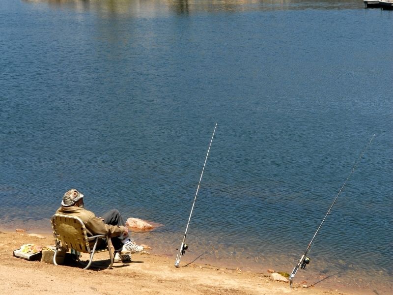 man sitting on chair with two fishing poles at big bear lake in summer