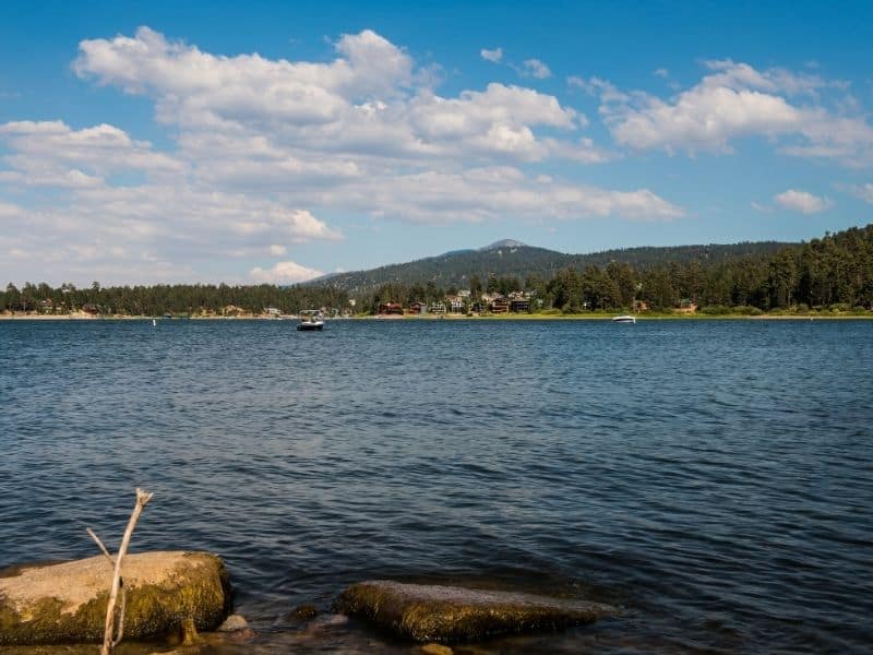 the calm waters of big bear lake in summer with two boats on the water on a partly cloudy day.