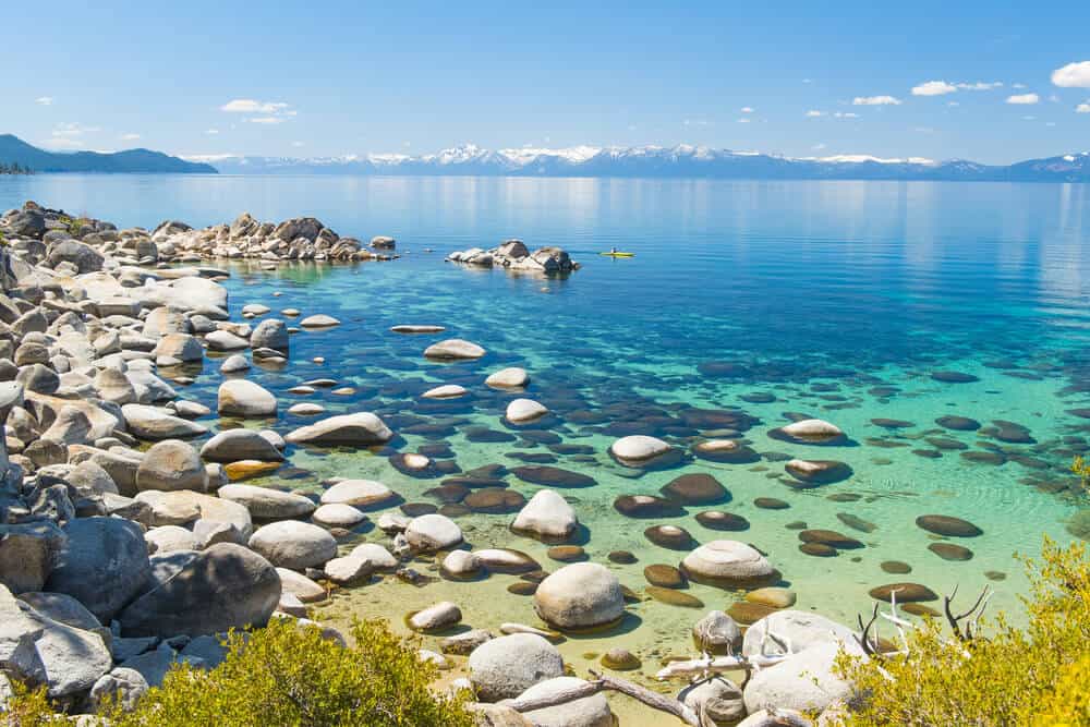 rock-strewn waters of lake beach at hidden beach near incline village in north tahoe beach. kayaker in the distance in blue-green waters