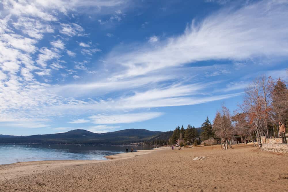 the sandy beach in tahoe in kings beach surrounded by fall trees and a cloudy sky with one person visible on the beach