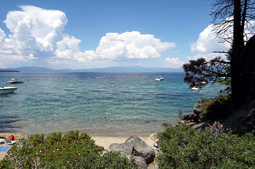 rocks on a sandy beach at lake tahoe with boats off in the distance and clouds on the horizon