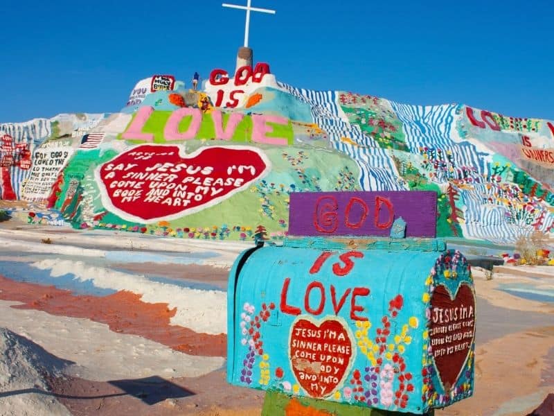 colorful painted mountain and mailbox of salvation mountain with phrases such as 'god is love' and 'jesus I'm a sinner' written on it in block letters