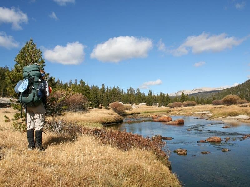 a hiker with a backpack standing by a creek in tuolumne meadows hiking alongside the john muir trail