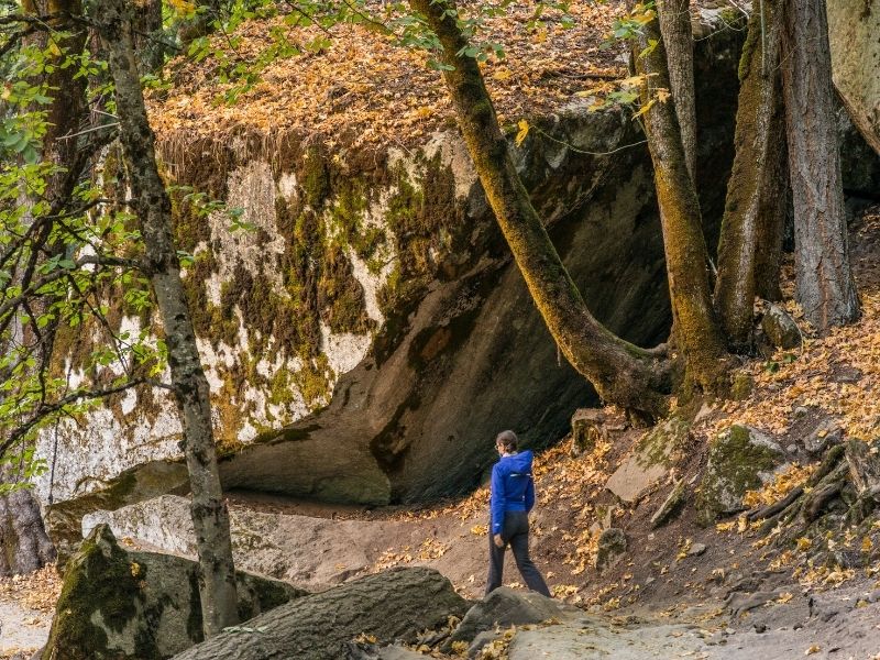 woman in a blue jacket walking the yosemite loop trail amidst trees and large rocks