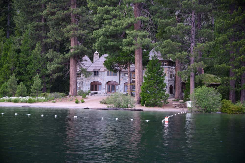 sandy beach in lake tahoe in front of a castle made of stone influenced by Scandinavian design in the middle of a pine forest