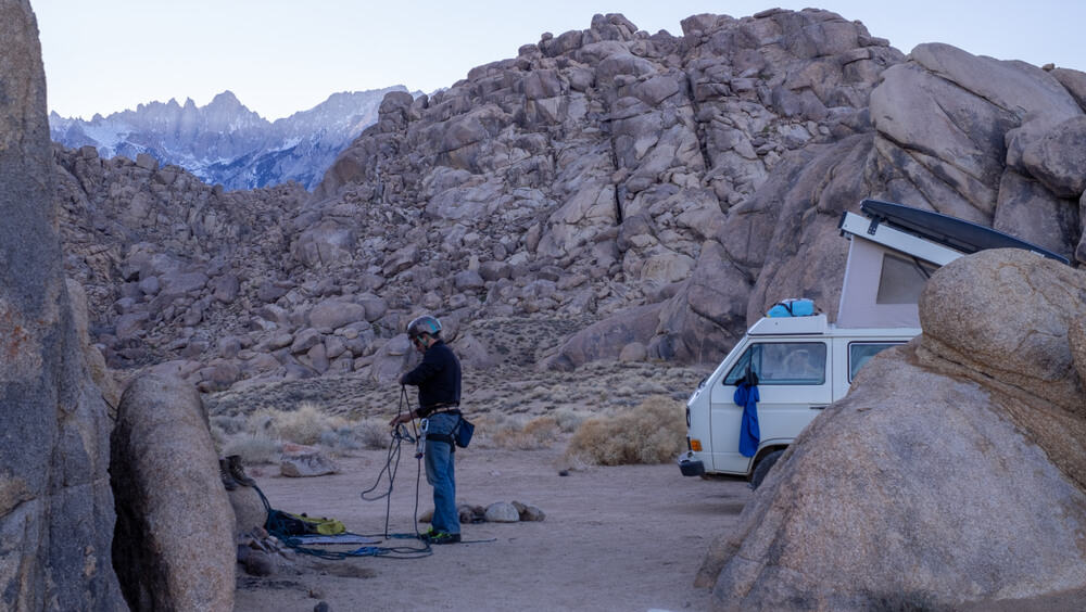 Climber coiling the rope and wearing climbing gear on a rocky environment with a camper van at Alabama Hills, California.