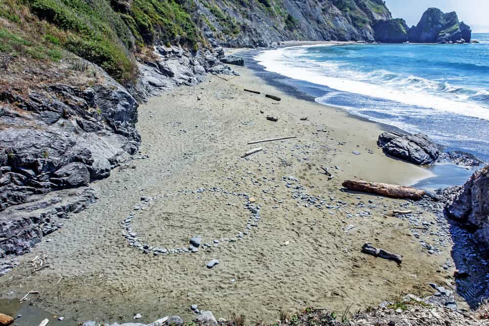 Walking down an old secluded beach trail, perched high on a steep jagged cliff, you see blue & aquamarine seas, surf crashing on a rocky / sandy Northern California beach at the end of Enderts trail.
