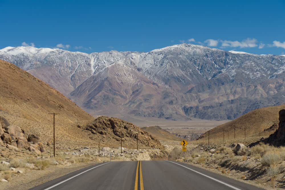 whitney portal road heading towards the alabama hills with enormous sierra nevada mountains looming over the road