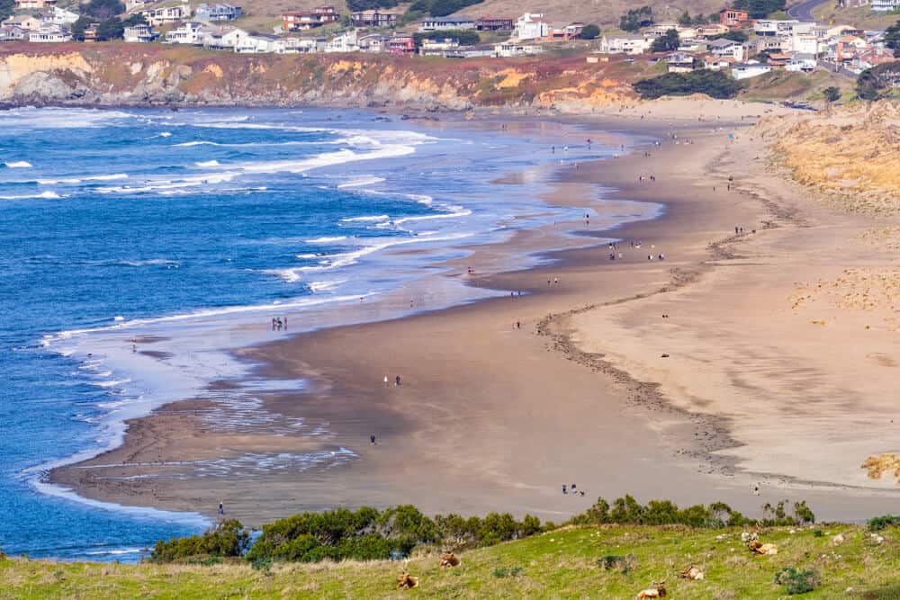 beach with people on it seen from above with houses in the distance.