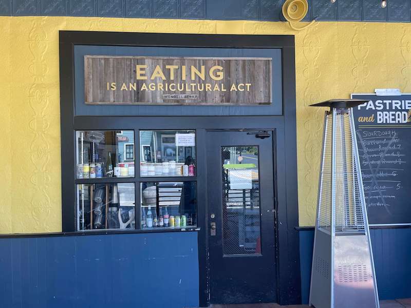 sign that reads 'eating is an agricultural act' on a yellow wall