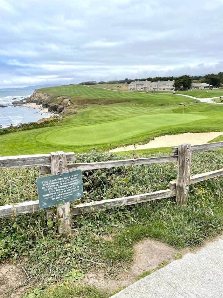 View of the historic 18th hole of the Old Course of the Half Moon Bay Golf Links with an information sign and the Pacific Ocean in the background.