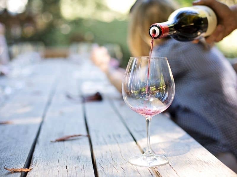 a hand pouring a glass of red wine at a napa wine tasting while sitting at a large outdoor table