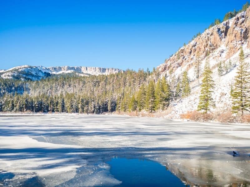 view from one of the lakes of mammoth lakes in winter, partially frozen over with snow on the ground