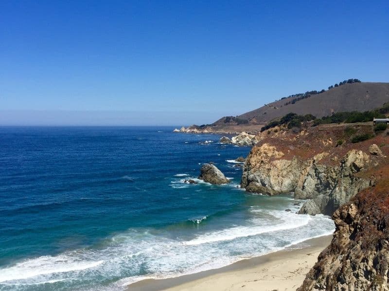 dark blue water and fine sand on the shores of big sur coastline of california on a sunny day with no fog