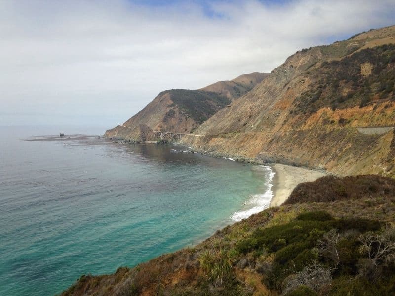 Big Sur on a partially cloudy day with brilliant turquoise water and the bridge visible in the far distance