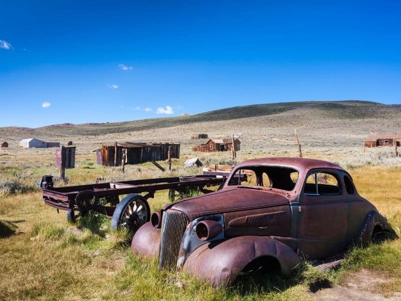 A rusted car, an old wagon, and old buildings abandoned to time in Bodie Ghost Town in California