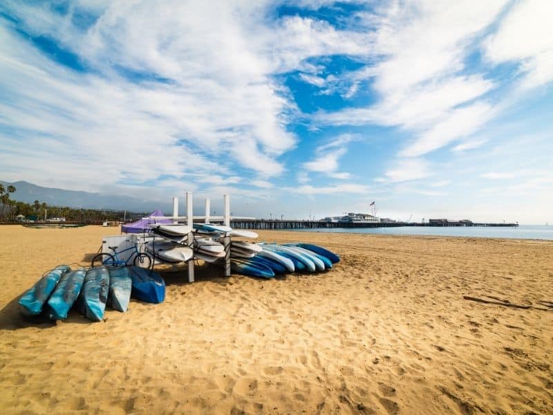 a stack of kayaks piled up for rent on the sandy beach near santa barbara, a beautiful kayaking spot in southern california