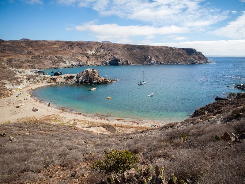 a peaceful bay with a half-moon beach in catalina island, with three small boats and a kayak out in the water