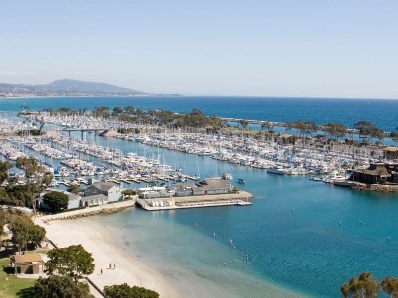 the soft white sand and blue waters of dana point california with harbor and boats nearby it -- a great launch for kayaking in southern california