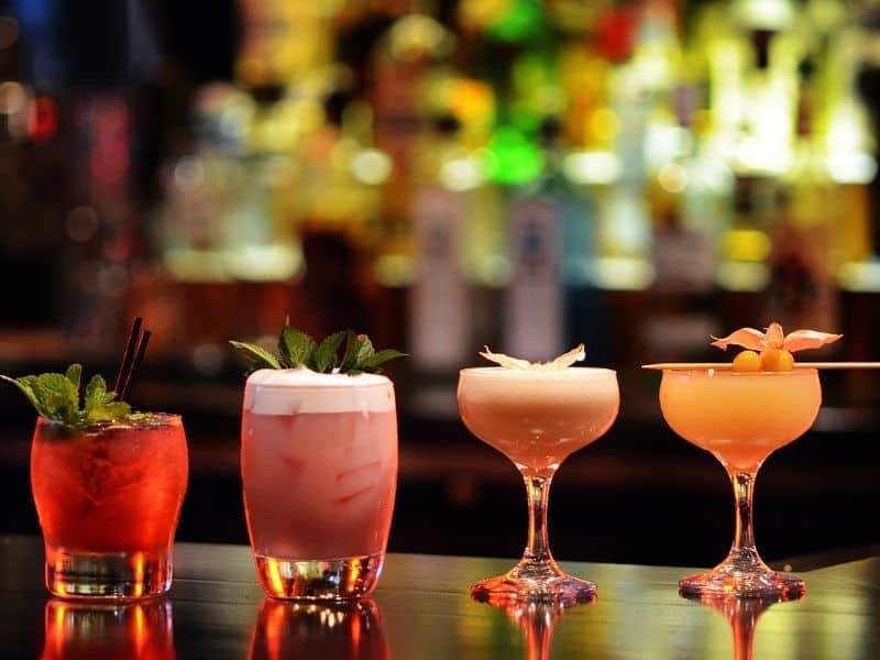 a selection of four pretty cocktails lined up in a row on the bar edge