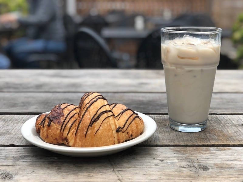 a croissant drizzled with chocolate and an iced chai latte drank outside on a picnic table