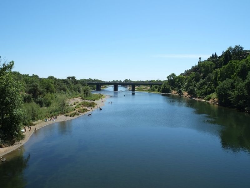 view from above on a bridge looking at the Sacramento river with. abridge in the distance and a few people in the water