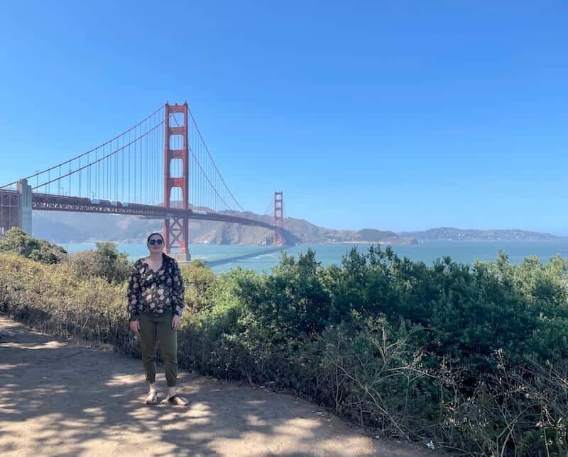 Allison standing with a view of the Golden Gate Bridge behind her and shrubbery on a trail walking to the bridge