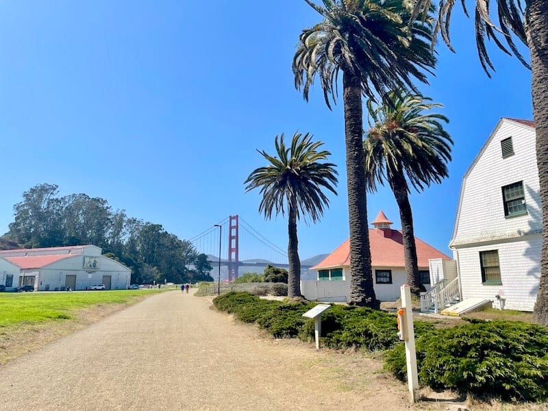 walking down the scenic crissy field promenade with palm trees and old military buildings with a view of the golden gate off in the distance at the end of the path