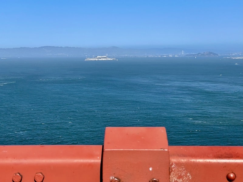 alcatraz island just barely visible in the distance with the railing of the golden gate in the frame