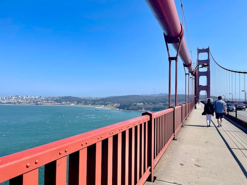 walking across the golden gate bridge with the pedestrian walkway and the typical red spanning suspension bridge architecture with art deco detailing