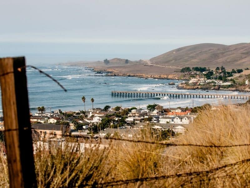 the town of cayucos seen from a hill above the town with the historic pier and beach visible