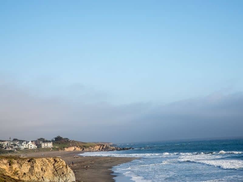 the coastline of cambria with some beach houses visible in the distance as waves lap the central coast shoreline on this drive from los angeles to big sur