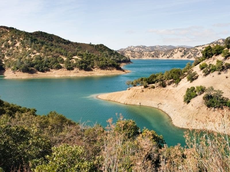 blue waters of lake berryessa with some brush and dry ground