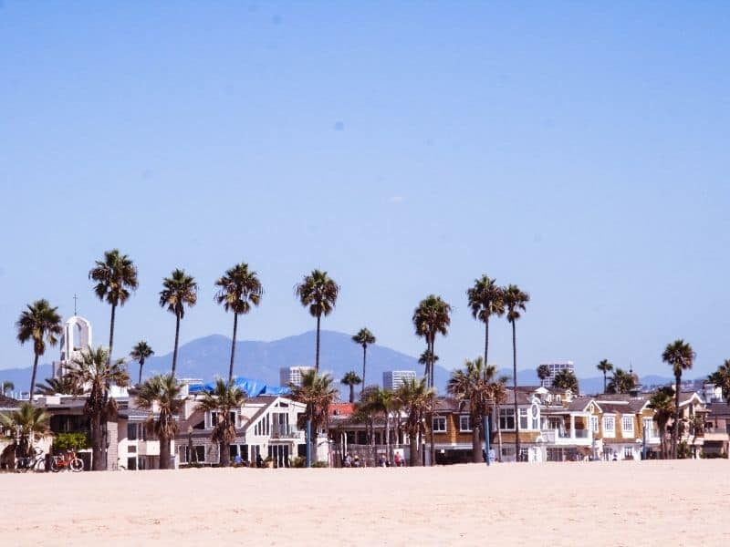 the beach at newport beach with houses, palm trees and a mountain behind in the distance