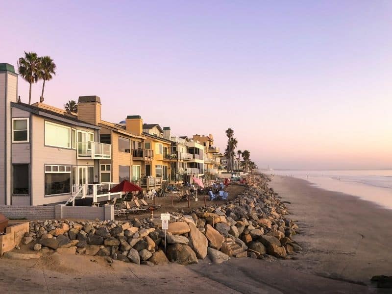 beach houses on the shore of oceanside with a pinkish purple sunset in the distance