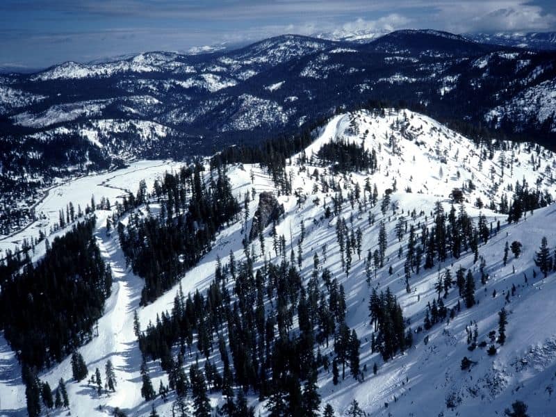 snow covered mountains with a ski run through it and trees beside it