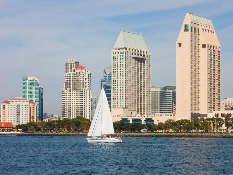 sailboat in the water in front of san diego skyline buildings ascending in height from left to right